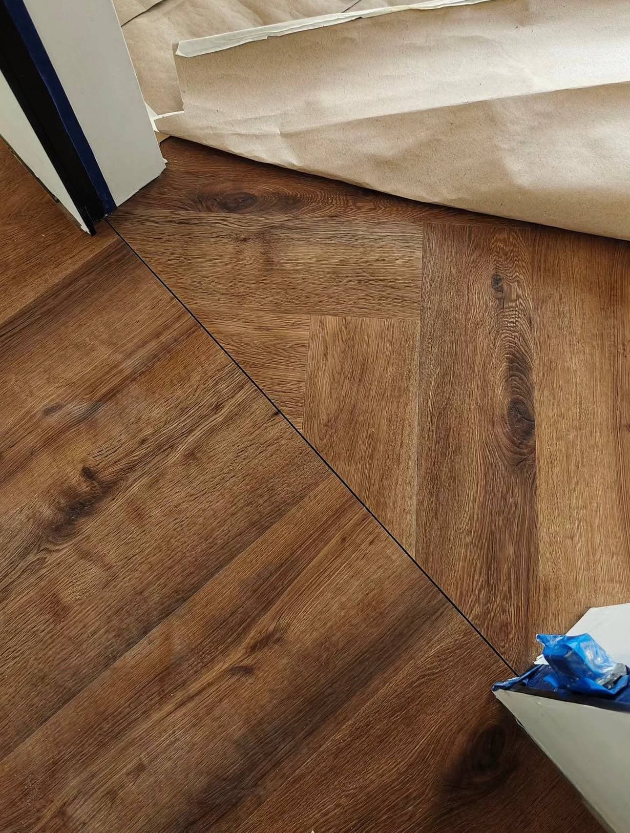 Cameră goală cu laminat deschis în spic și materiale de montaj lângă perete